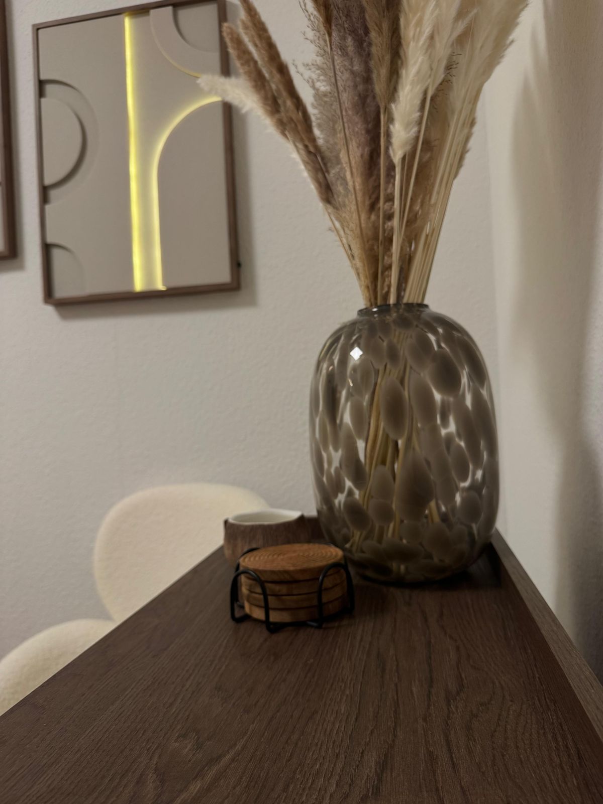 Dekoration im Studio: Glasvase mit Pampasgras vor einem Wandbild mit Bögen